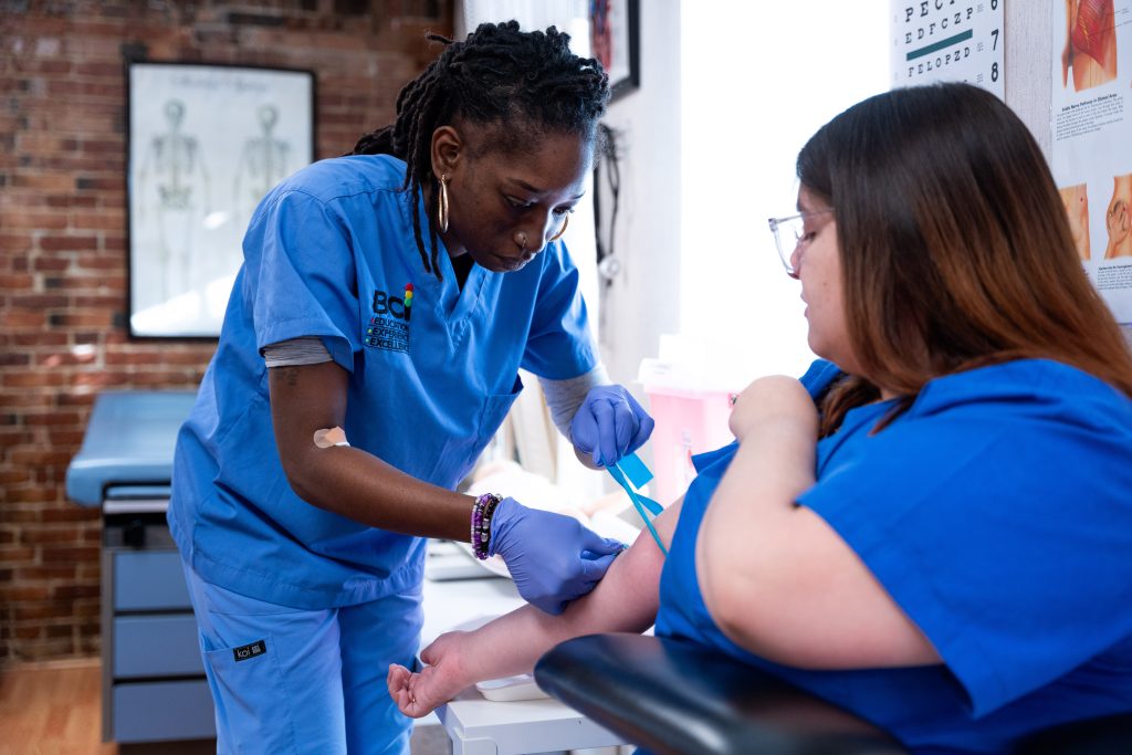 Phlebotomist drawing blood from seated patient